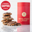 A red cylindrical canister with the logo 'RIVER STREET SWEETS' on it, alongside stacked chocolate bear claws candies with pecans and caramel visible on top.