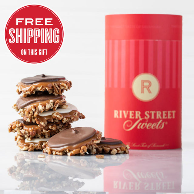 A red cylindrical canister with the logo 'RIVER STREET SWEETS' on it, alongside stacked chocolate bear claws candies with pecans and caramel visible on top.