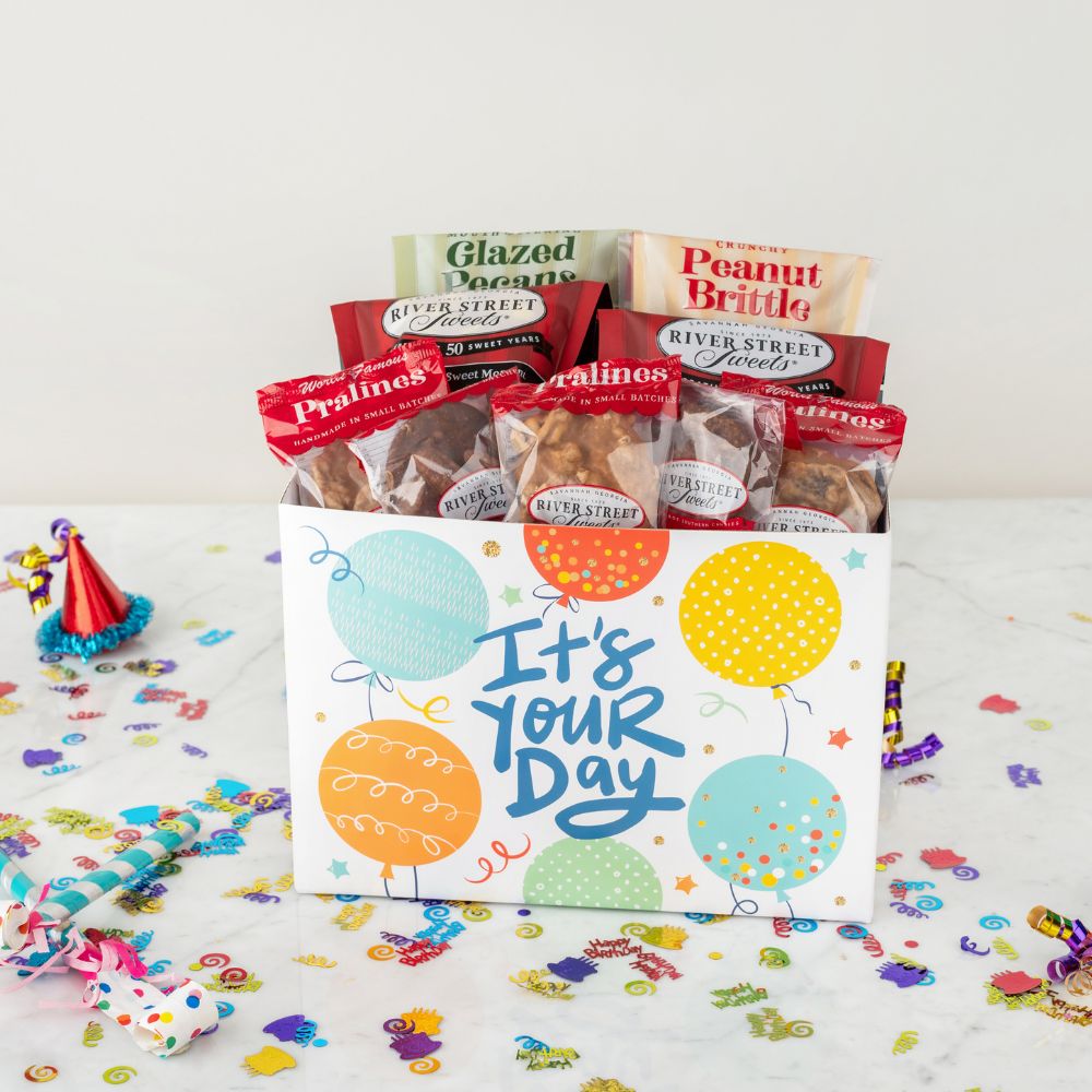 Gift box with snacks and a card saying 'It's Your Day' on a celebratory background.