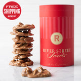 A red cylindrical candy canister labeled 'River Street Sweets' with a stack of praline candies in front of it,