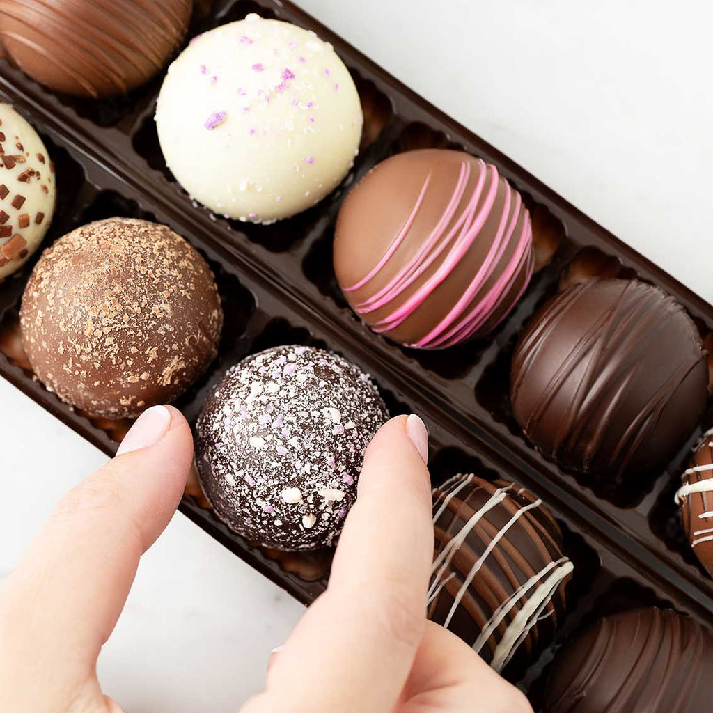 Assorted chocolate truffles in a box with a hand reaching for one.