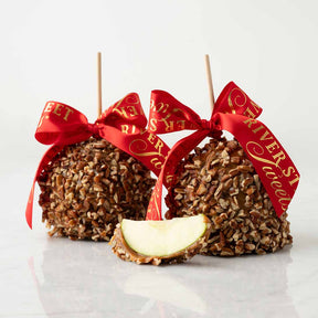 Two caramel apples with pecans and red ribbons on a white background