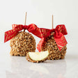 Two caramel apples with nuts and a red ribbon on a white background