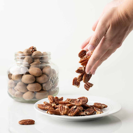 Hand picking pecans from a jar and plate on a white background