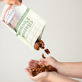 Person pouring glazed pecans from a bag onto their hand against a white background