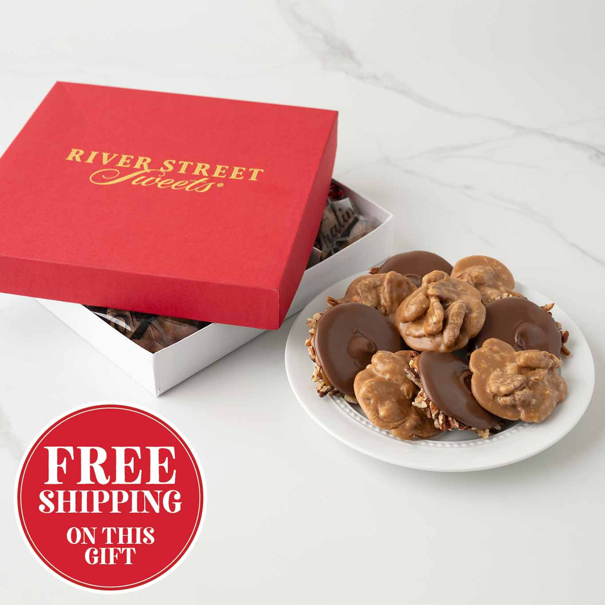 Red gift box with 'River Street Sweets' branding, a plate of chocolates and pralines on a white background with a free shipping banner