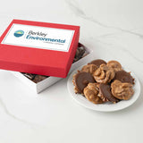 Red gift box with custom logo next to a plate of chocolate-coated bear claws and pralines on a white surface.