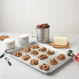 Baking tray with pralines, measuring cups, and ingredients on a marble countertop.
