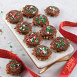 A tray of festive sprinkle topped milk chocolate bear claws with red and green holiday sprinkles, presented with a red ribbon.
